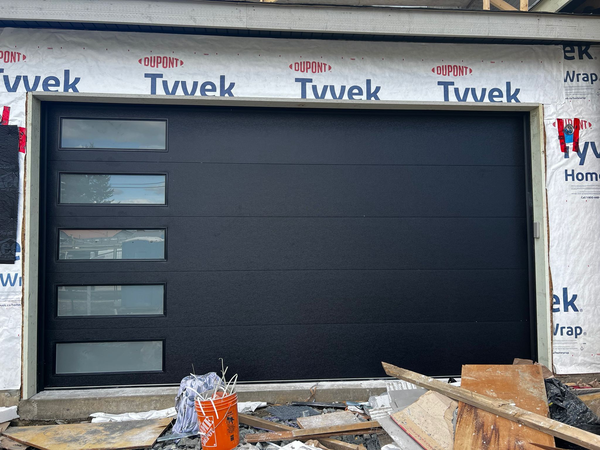 New sectional garage door installed during a home construction project, house wrap visible above.
