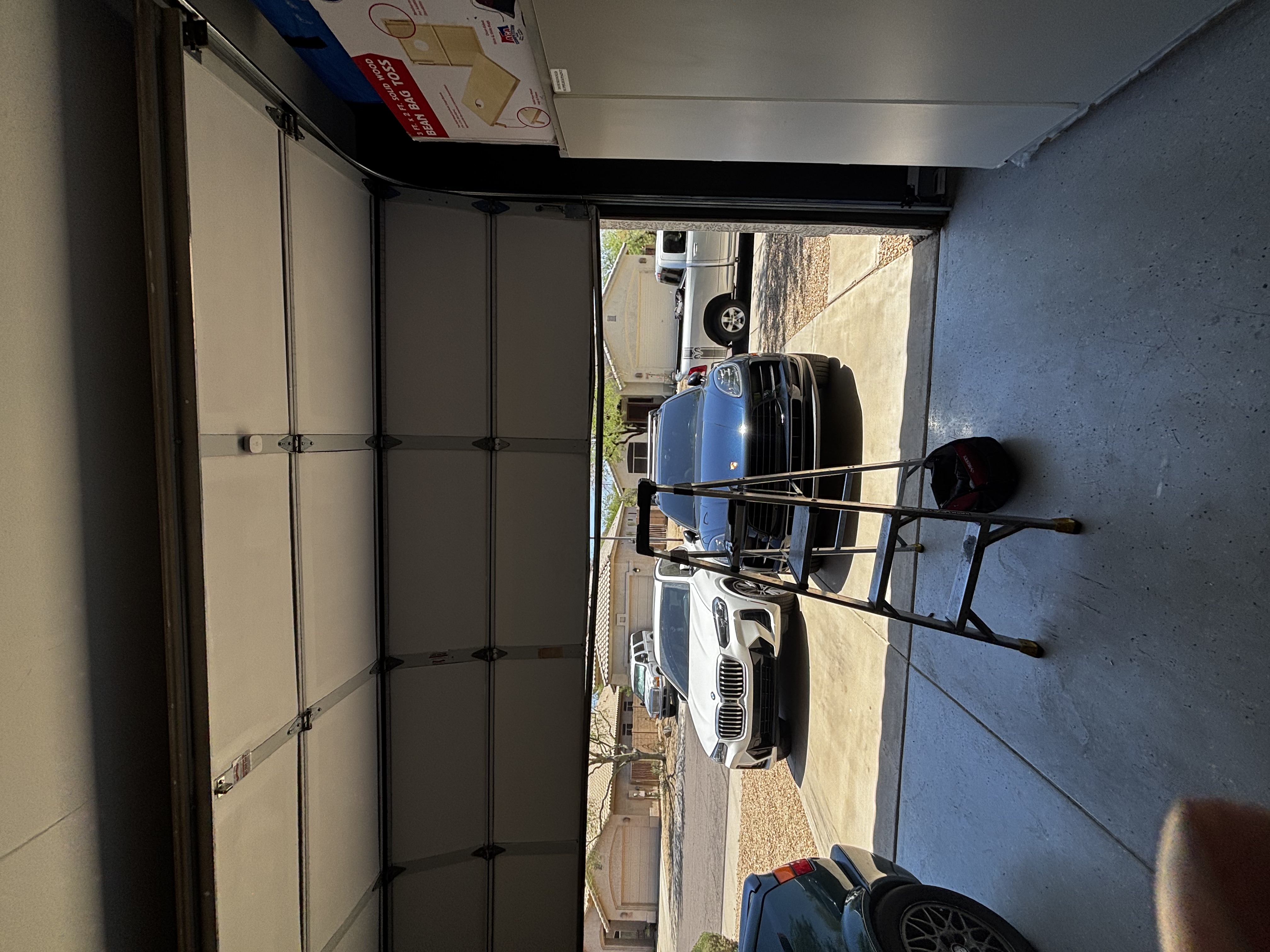 Technician on a ladder installing garage door track hardware in an open garage.