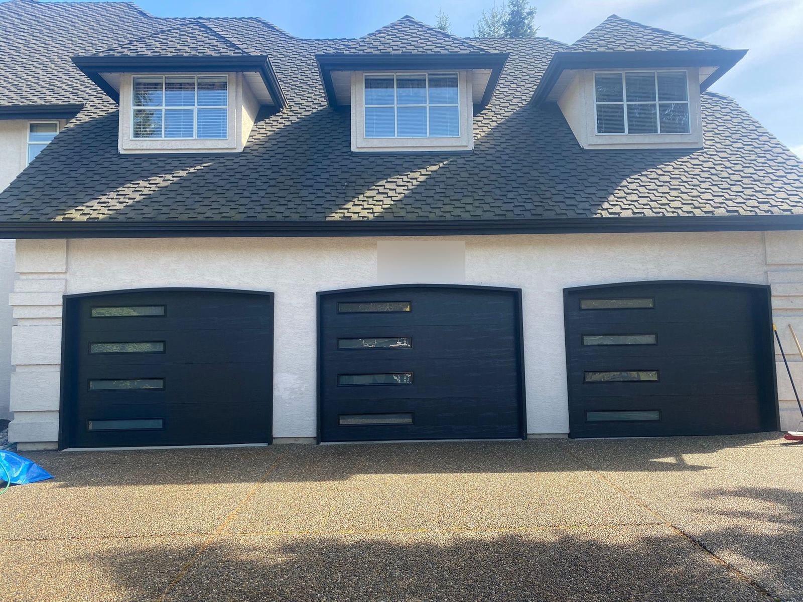 Three dark carriage-style garage doors with window inserts on a two-story home.